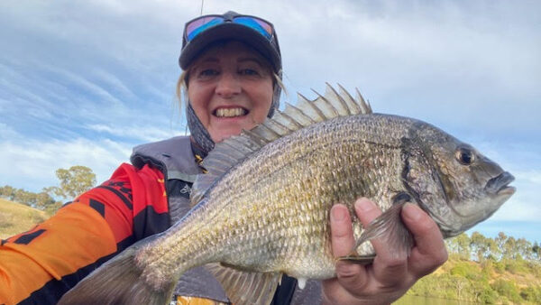 A woman wearing a red and orange shirt is holding a Bream fish for a photo selfie style